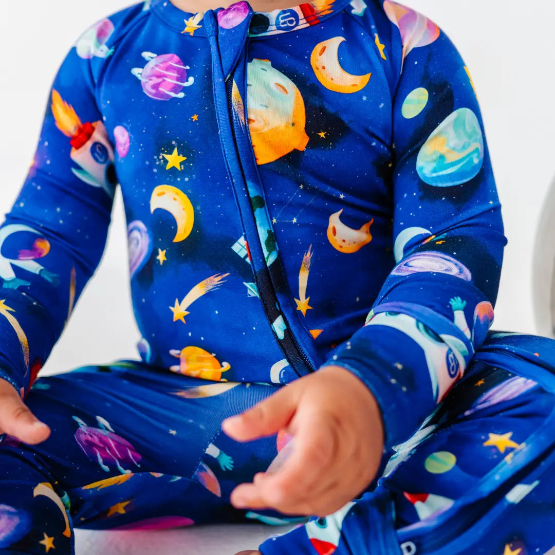 Close-up of a baby sitting in a royal blue zip-up pajama printed with planets, moons, rockets, and shooting stars.